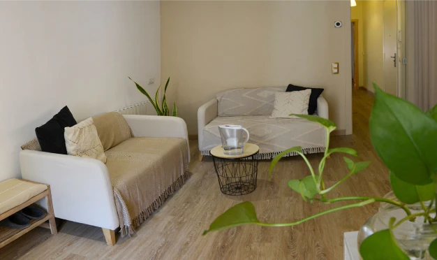 Zona de entrada con sofás confortables, luz cálida y detalles naturales, diseñada para recibirte con calma y cercanía antes del masaje.